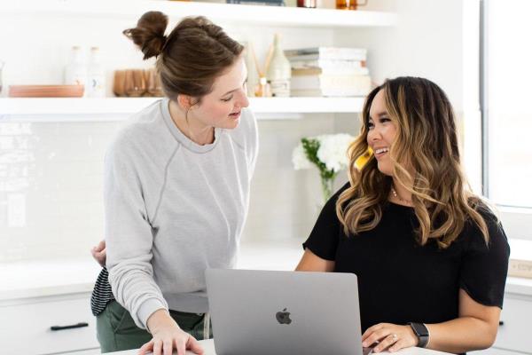 Professional women smile and discuss information on laptop
