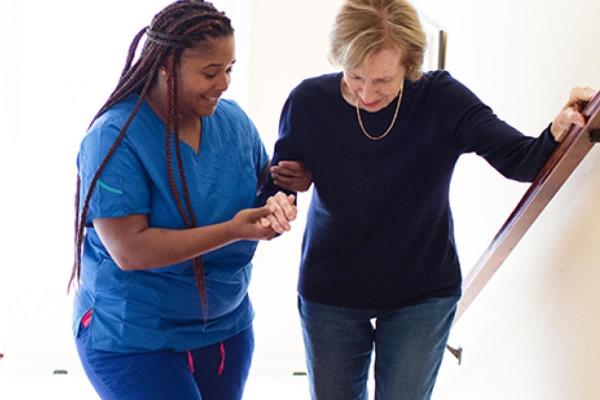 Care Professional helps aging woman up the stairs