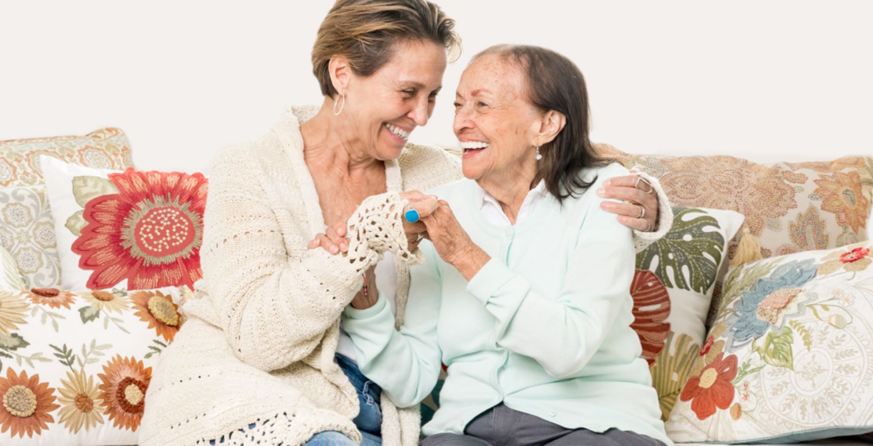 Aging and younger woman laugh and embrace in hug on sofa