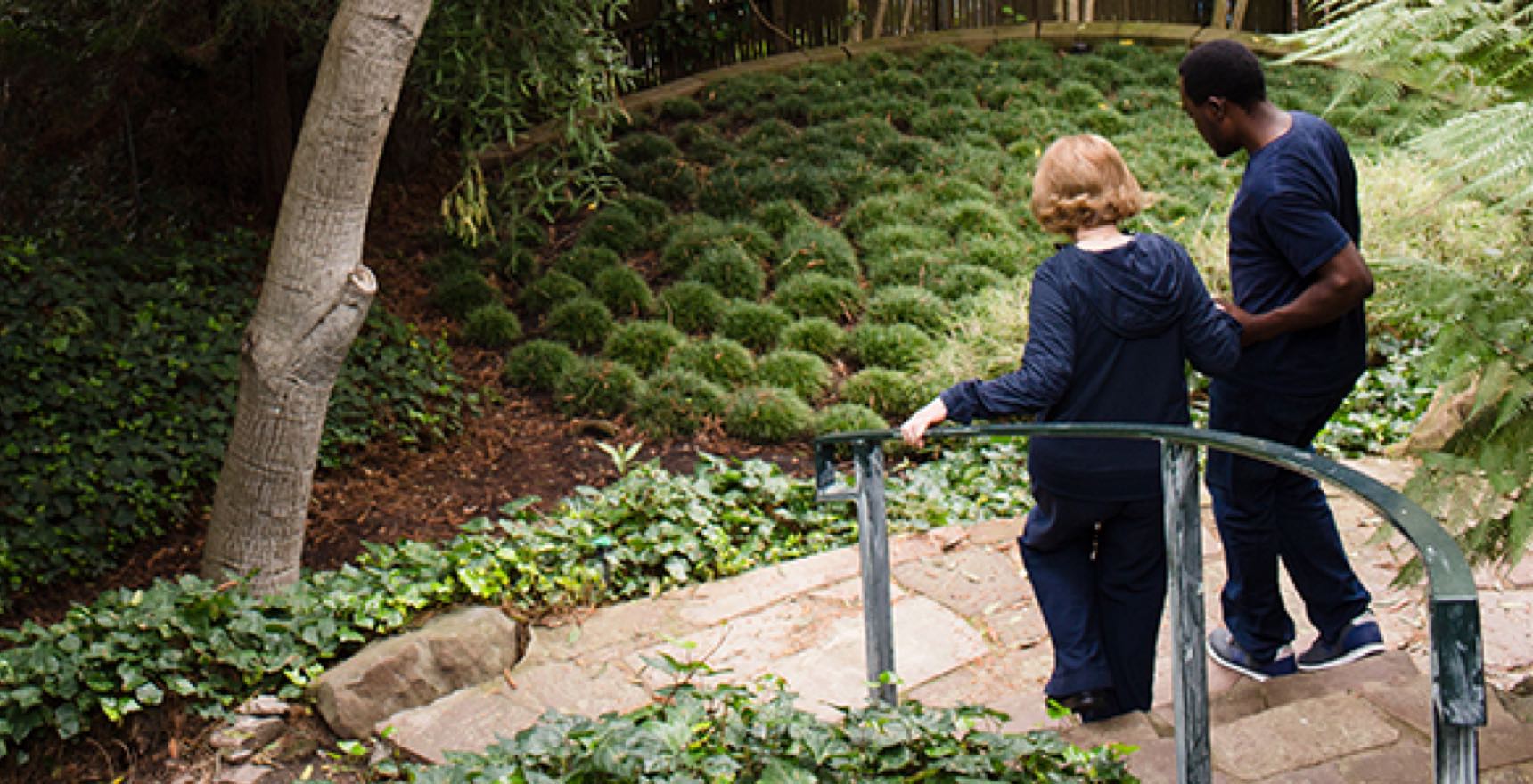 Care Professional helps aging woman down the stairs to garden