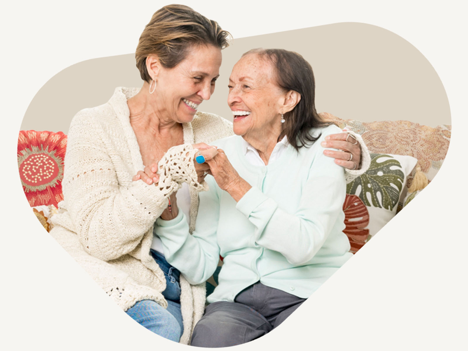 Aging woman and care professional laugh together on a couch at home