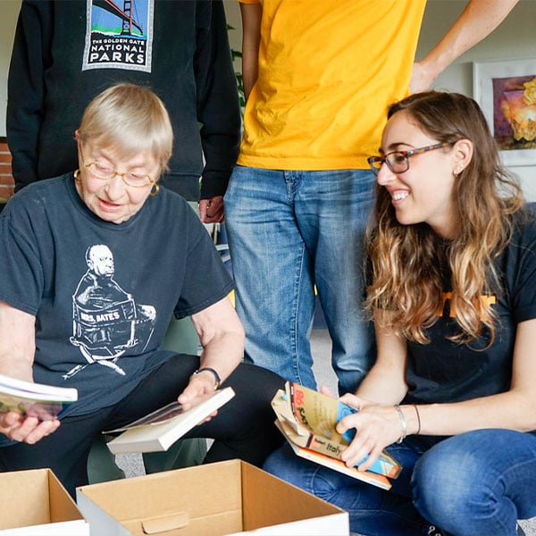 Aging woman and younger group of adults happliy look through a box of books