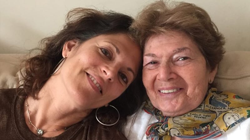 Aging mother and daughter sit smiling together on sofa