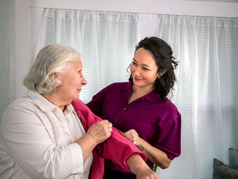 Home Instead caregiver assists aging woman walking with cane