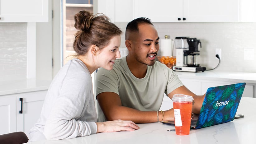 Honor engineers smile while reading from laptop in kitchen