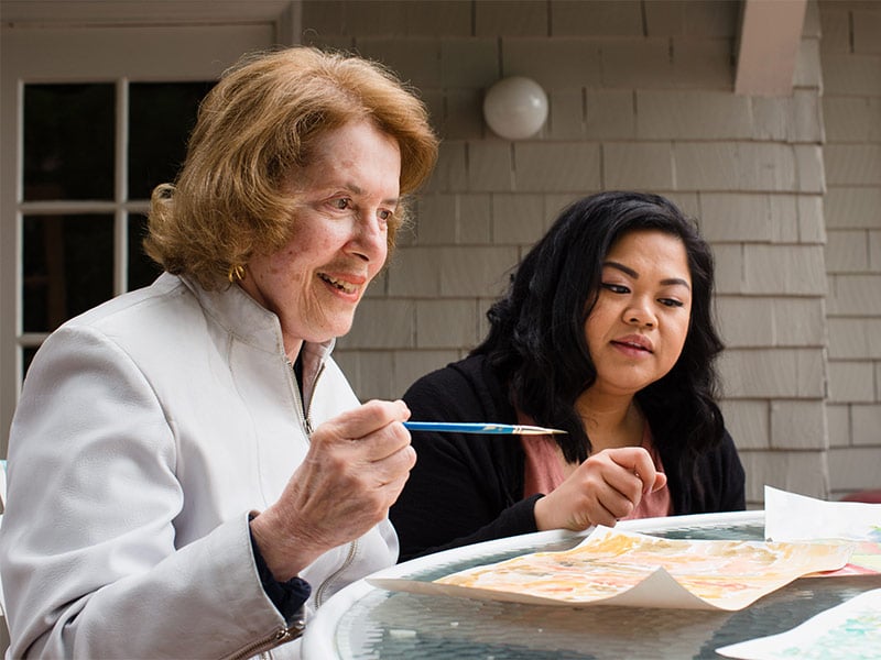 Aging woman and care professional paint together outside