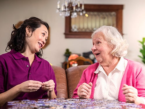 Aging woman and care professional work on puzzle together at home