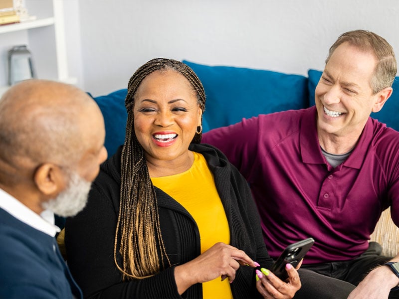 Care Professionals talk and laugh with aging man while sitting on sofa