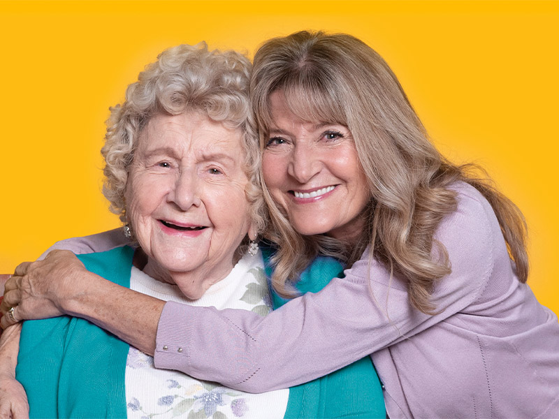 Aging mother and daughter smile while sharing a hug