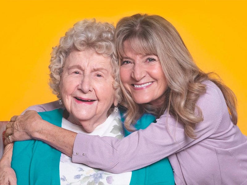 Aging mother and daughter smile while sharing a hug