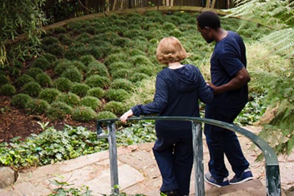 Care Professional helps aging woman down the stairs to garden